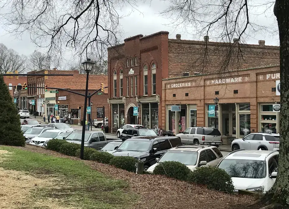 Two-story brick storefronts on South Main Street in downtown Waxhaw, with old painted wall signs reading Groceries and Hardware, lamp posts and parked cars